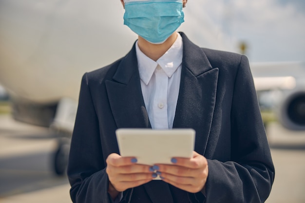 Foto ritagliata di una donna con una maschera protettiva che tiene il suo tablet con due mani