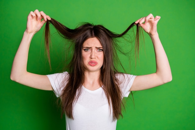 Foto ritratto di donna offesa indossare t-shirt bianca tenendo i capelli braccia estremità asciutte isolato sfondo di colore verde