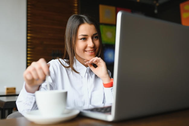 Foto ritratto di splendida donna attraente che lavora al computer portatile digitando seduto al bar a bere caffè