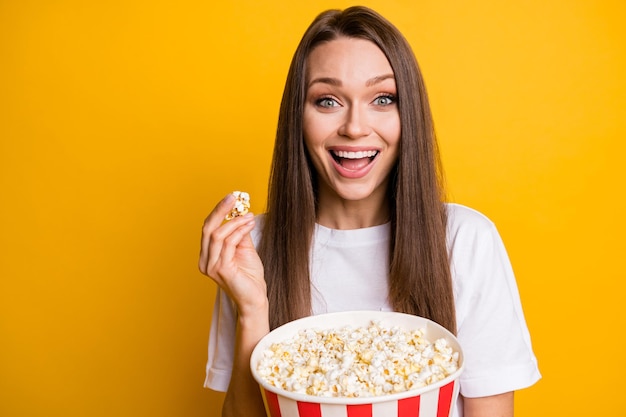 Foto ritratto di una ragazza che ride felice che mangia pop corn guardando un film comico al cinema ha isolato uno sfondo di colore giallo vibrante