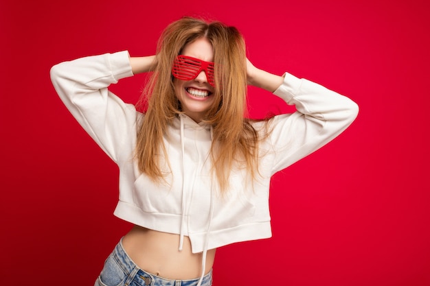 Foto scattata di bella giovane donna bionda positiva che indossa abiti casual e occhiali ottici alla moda