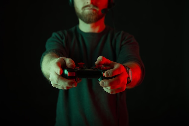 Foto senza volto di un uomo con la barba che indossa le cuffie e gioca con il joystick Sfondo scuro e luce rossa
