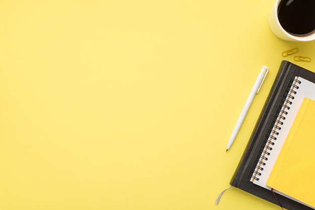 Foto sopra di una tazza di caffè con penna per notebook e graffette isolate su sfondo giallo