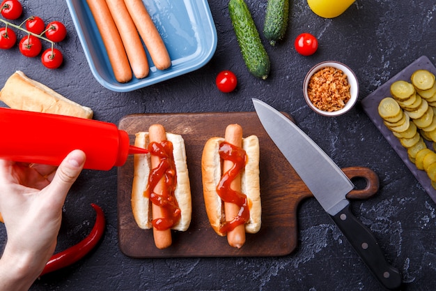 Foto sopra il tavolo con ingredienti per hot dog, tagliere, mani dell'uomo