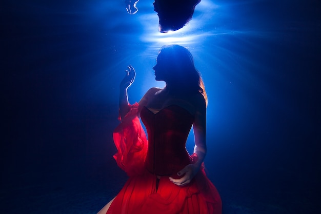 Foto subacquea di sagoma bella ragazza con i capelli lunghi scuri che indossa un vestito rosso