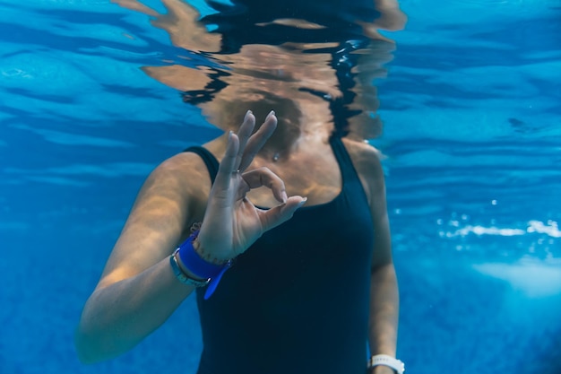 Foto subacquea in una piscina una ragazza in costume da bagno mostra un segno ok con la mano