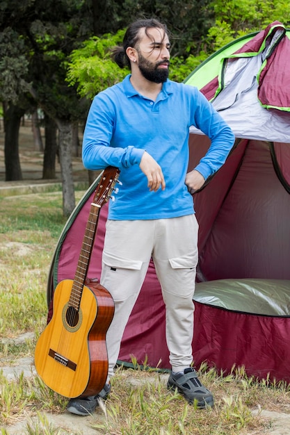 Foto verticale del giovane che tiene la chitarra e in piedi davanti alla tenda