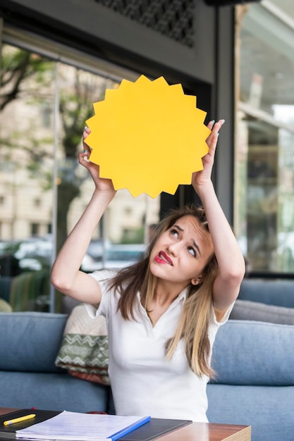 Foto verticale della giovane bionda che tiene la scheda idea in cima alla sua testa e la guarda