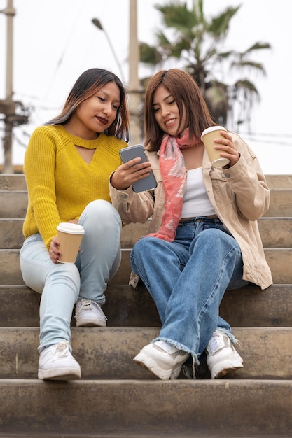 Foto verticale di amici che bevono un caffè mentre usano un cellulare per strada