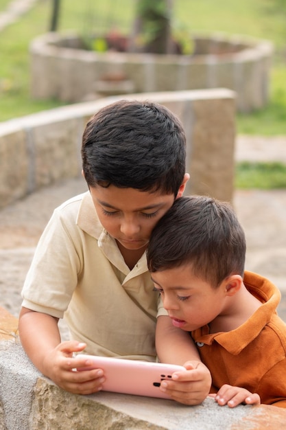 Foto verticale di bambini e fratelli con bisogni speciali assorbiti dal telefono in un ambiente naturale