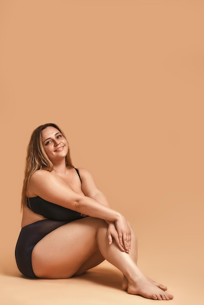 Foto verticale di donna paffuta di modella sexy plus size in lingerie nera seduta sul