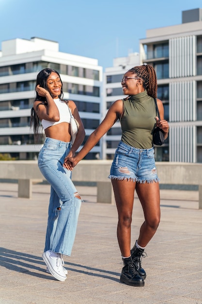 Foto verticale di due giovani amici africani passeggiano felici tenendosi per mano in città, concetto di amicizia e stile di vita urbano