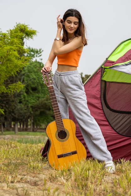Foto verticale di giovane bella signora che tiene la chitarra e allunga i capelli al campeggio