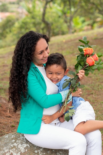 Foto verticale di madre e figlio felici che si godono la natura e le rose per la festa della mamma