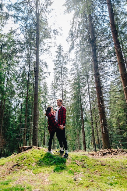 Foto verticale di una bella coppia di hipster nei boschi che si abbracciano e parlano su uno sfondo di splendidi panorami La coppia si sta attivamente rilassando nella foresta di montagna