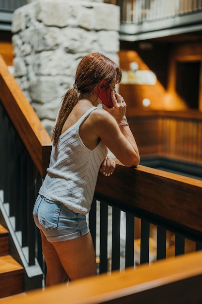 Foto verticale di una donna che parla al cellulare sulle scale di legno di un hotel