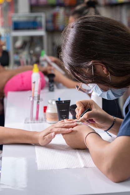 Foto verticale di una manicurista professionista che applica una mano di fondo trasparente alle unghie di una donna