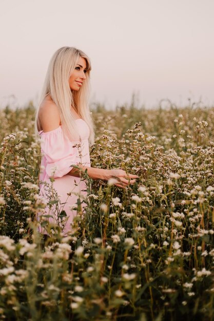 Foto verticale donna bionda in posa nel grande campo infinito di margherite in serata estiva