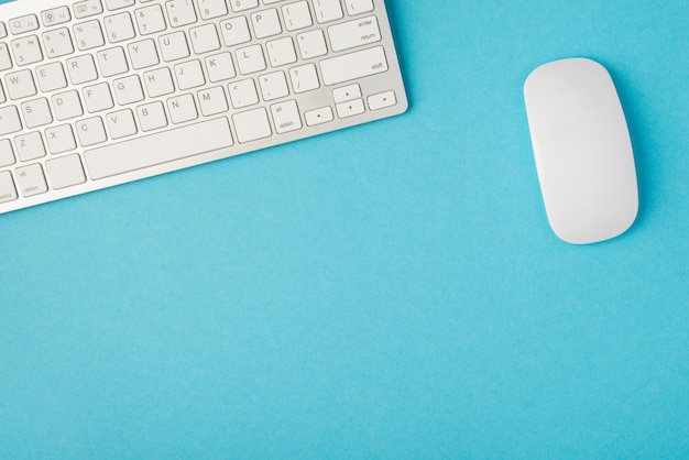 Foto vista dall'alto del desktop con tastiera e mouse bianchi su sfondo blu isolato con spazio vuoto