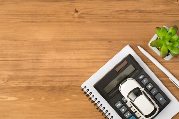 Foto vista dall'alto del posto di lavoro con modello di auto con pianta a penna e calcolatrice su notebook su sfondo di tavolo in legno isolato con copyspace