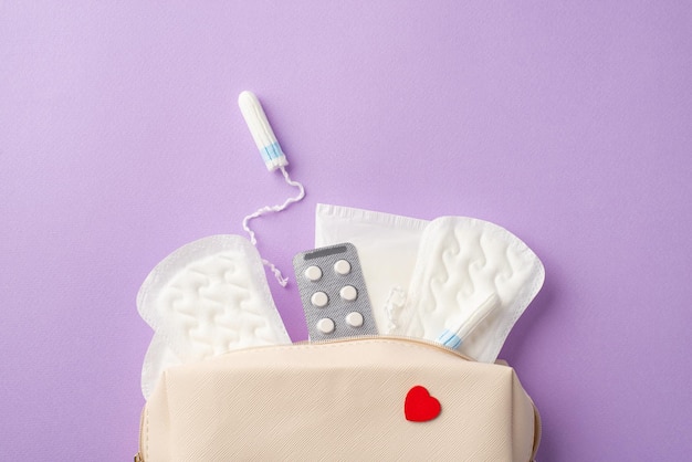 Foto vista dall'alto della borsa medica aperta con tampone igienico e piatto di pillole su sfondo viola pastello isolato