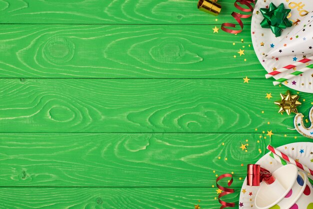 Foto vista dall'alto della composizione della festa di compleanno a destra con nastro dorato verde stelle cappello paillettes tubi pois bicchieri di carta e piatti su sfondo tavolo in legno verde isolato con copyspace