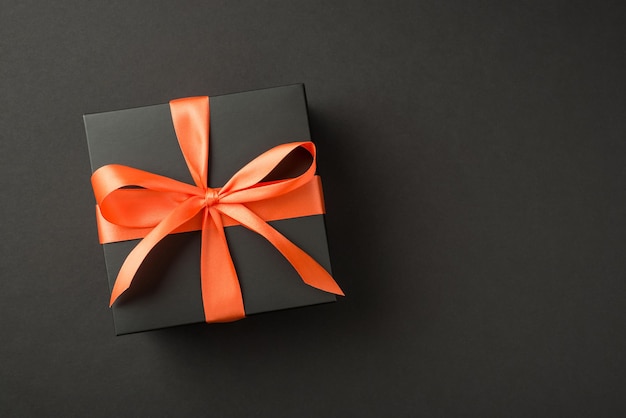 Foto vista dall'alto della confezione regalo nera con fiocco di nastro di raso arancione su sfondo nero isolato con copyspace