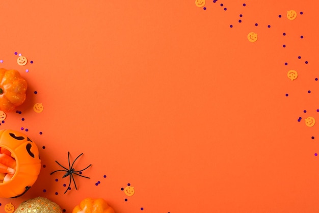 Foto vista dall'alto di decorazioni di halloween cesto di zucca con ragno di mais caramelle sagome di zucche piccole arancioni e dorate e coriandoli viola su sfondo arancione isolato con copyspace