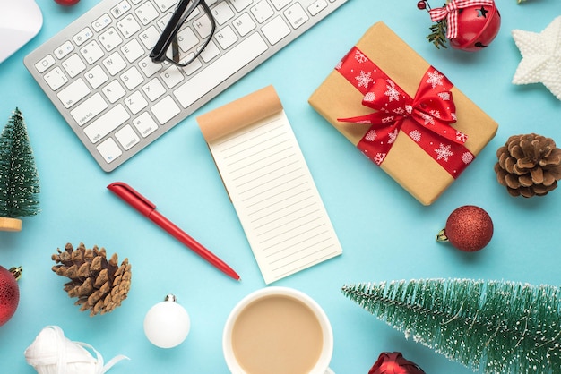 Foto vista dall'alto di notebook penna occhiali tastiera mouse tazza di bere caldo giocattoli di pino albero di natale palle coni stella bobine di campana di nastro giftbox su sfondo blu pastello isolato con spazio vuoto