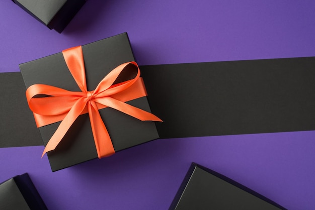 Foto vista dall'alto di una confezione regalo nera con scatole di fiocco di nastro arancione su sfondo viola e nero isolato con copyspace