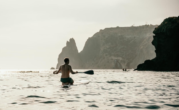 Foto vista laterale di un uomo che nuota e si rilassa sulla tavola da sup uomo sportivo in mare sullo stand