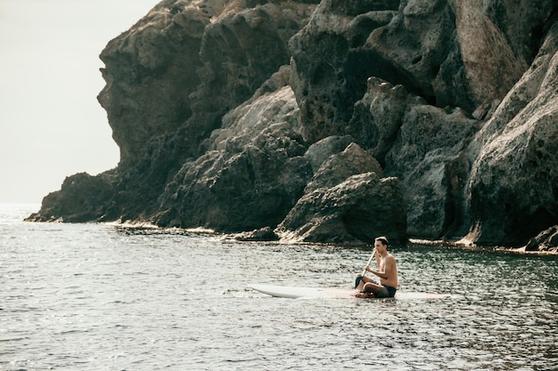 Foto vista laterale di un uomo che nuota e si rilassa sulla tavola da sup uomo sportivo in mare sullo stand