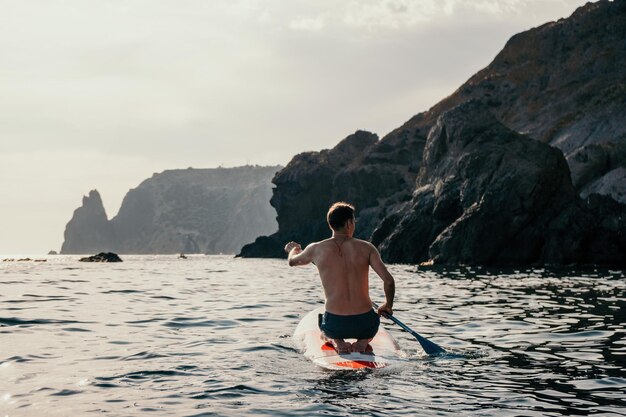 Foto vista laterale di un uomo che nuota e si rilassa sulla tavola da sup uomo sportivo in mare sullo stand