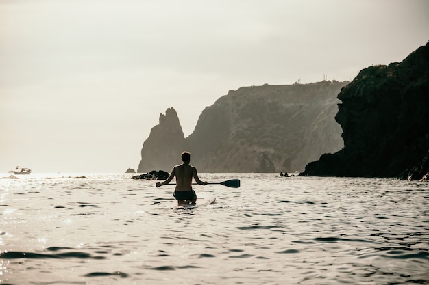 Foto vista laterale di un uomo che nuota e si rilassa sulla tavola da sup uomo sportivo in mare sullo stand