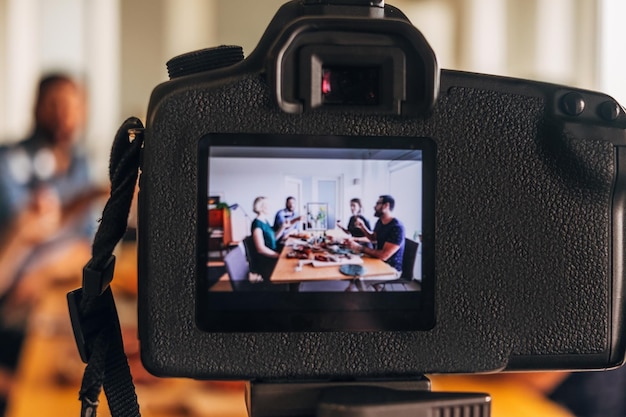 Fotocamera che registra persone blogger di cibo che mangiano e bevono attorno a un tavolo