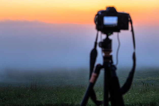 Fotocamera digitale nera su treppiede che riprende un paesaggio mattutino nebbioso in estate con messa a fuoco selettiva