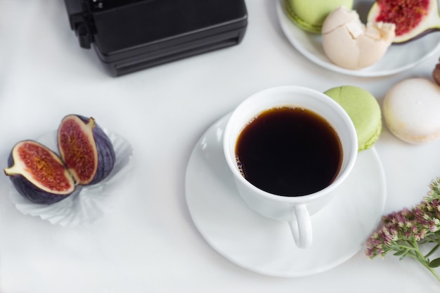 Fotocamera estetica flatlay tazze di caffè fichi e macaron su sfondo bianco vista dall'alto