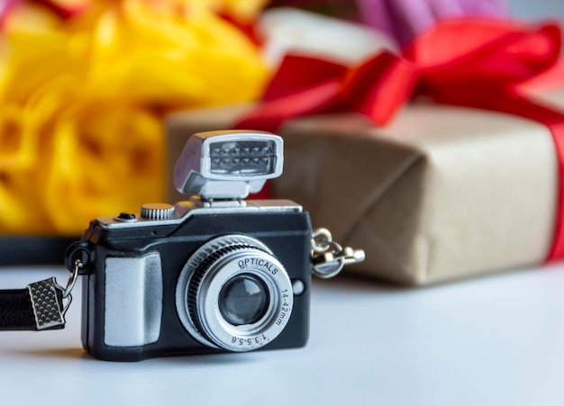 Fotocamera in miniatura sullo sfondo della confezione regalo e un mazzo di fiori Il concetto di fotografare il viaggio