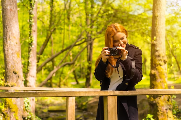 Fotografa donna con una giacca nera che si diverte in un parco autunnale, sorride e si diverte a scattare foto al tramonto