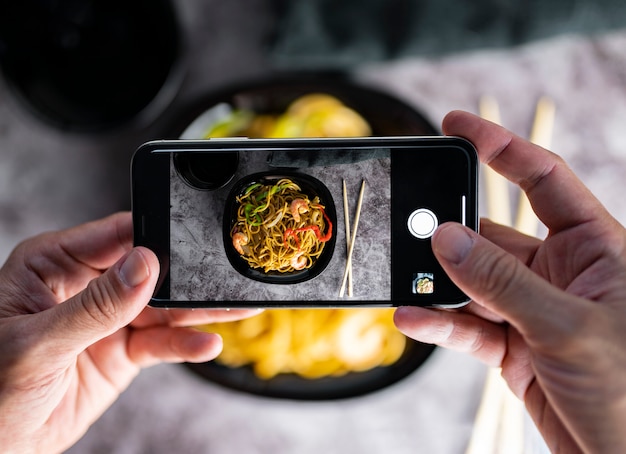 Fotografare il cibo. Mani che scattano foto di deliziosi spaghetti di verdure con lo smartphone