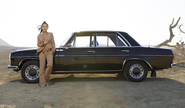 Fotografia all'aperto di giovane modella con auto nera nel deserto Foto di alta qualità