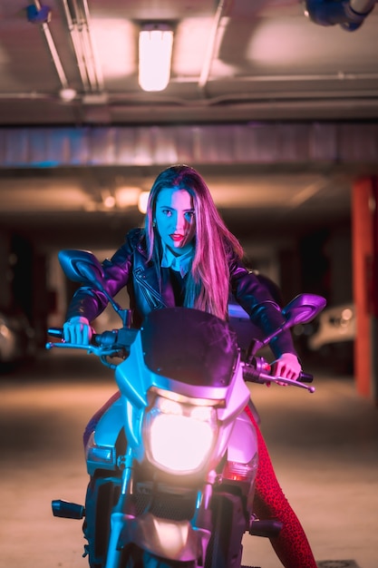 Fotografia con neon blu e rosa su una moto. Ritratto di un giovane modello biondo caucasico che indossa una giacca di pelle nera