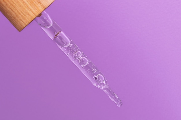 Fotografia del primo piano della pipetta con gel gocciolante. Copertura in legno zero rifiuti, sfondo viola. Concetto di mockup di cosmetici.