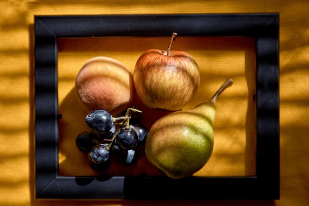 Fotografia di frutta creativa gruppo di uva mela pesca e pera nella cornice sotto ombre alla moda Vista dall'alto Vitamine concetto di cibo sano Foto di alta qualità