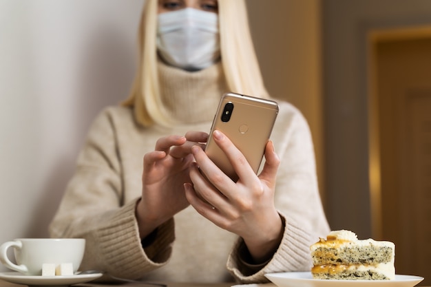 Fotografia frontale del telefono nelle mani di una ragazza con i capelli biondi sciolti, un maglione beige