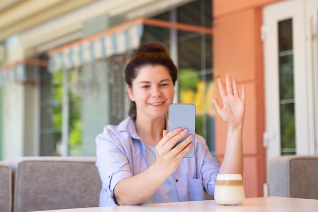 Fotografia ofdefocused donna allegra che tiene lo smartphone in mano e agita la mano