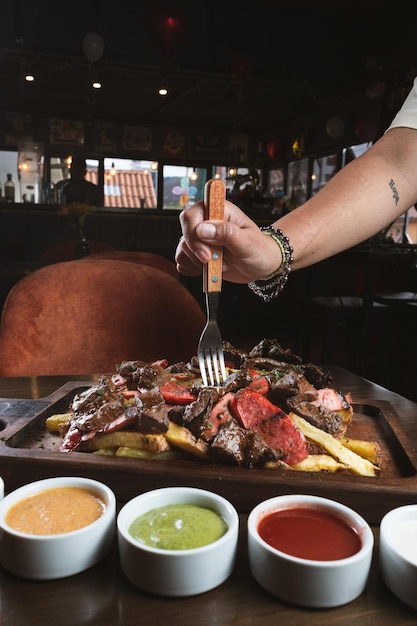 Fotografie di mani che mangiano una salchipapa mista al tavolo di una steakhouse