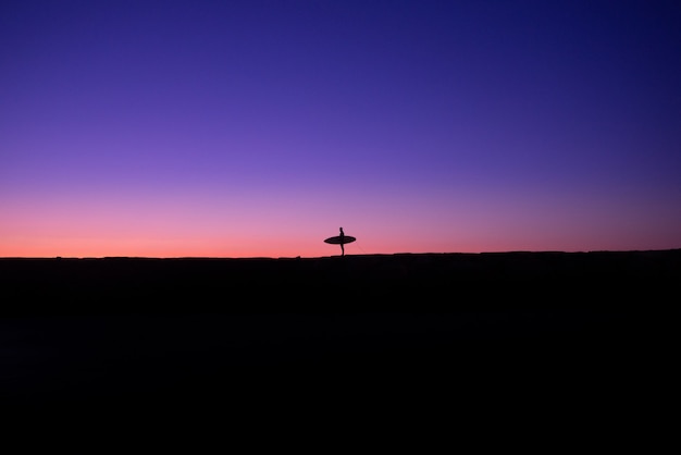 Fotografie minimaliste della silhouette di un surfista latino al tramonto su una spiaggia delle Hawaii