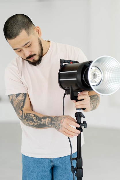 Fotografo asiatico professionista con tatuaggi eleganti che impostano l'illuminazione in uno studio moderno