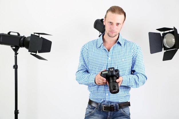 Fotografo bello con la macchina fotografica al lavoro sullo sfondo dello studio fotografico